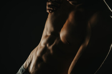 Close-up of a muscular male torso showing defined abs and chest muscles in a dark, dramatic setting.