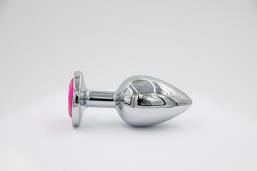 Obraz premium Close-up side view of metallic butt plug lying on white background. Soft focus. Sex shop display. Adult sex toys theme.