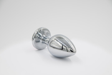 Close-up side view of metallic butt plug lying on white background. Soft focus. Sex shop display....