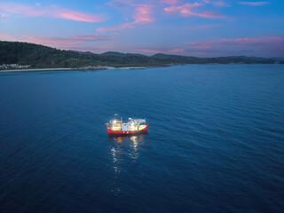 Illuminated fishing boat at night on calm blue waters. The vibrant red boat is anchored, casting light on its surroundings, creating a serene and tranquil scene. Ideal for maritime and nighttime theme