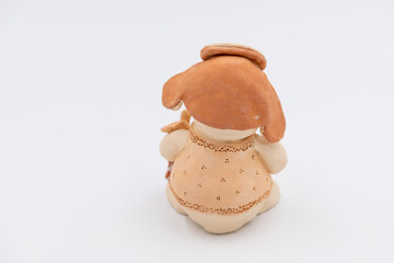 Close-up rear view of brown handmade ceramic snowman toy in hat with earflips holding smallChristmas tree on light grey background. Winter holidays present. Soft focus. Homemade gifts theme.