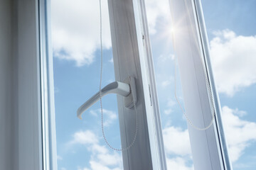 Close-up of a plastic PVC window with a white metal frame and handle, installed in a house, in a room in an apartment, view of the blue sky. household concepts. © Oleksandr