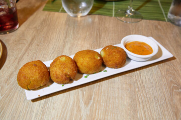 Sicilian arancini balls or risotto croquettes with tomato sauce on a white tray on a restaurant table