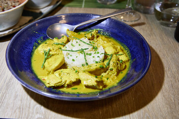 Chicken in coconut curry with white rice on a blue plate with spoon on a wooden restaurant table ready to eat