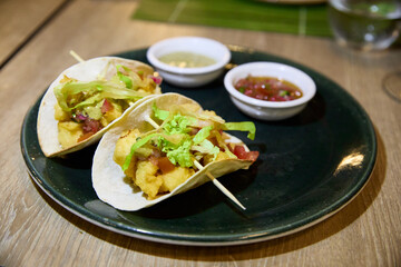 Baja California fish tacos skewered with lettuce, huacatay sauce and pico de gallo on a green plate on a wooden restaurant table ready to eat