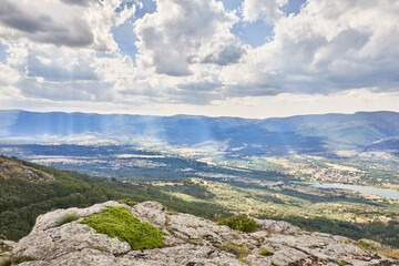 Beautiful landscape view of the Lozoya Valley, the town of Rascafría and the Pinilla reservoir from the top of the mountain, with clouds and sun rays, in the Guadarrama National Park, in Madrid, Spain