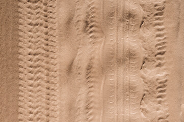 Background, texture of the uneven surface of traces, imprints from wheels, car tires on a sandy road. Photo, top view.