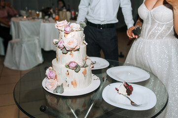 Photo of a large beautiful decorated three-tier cake against the backdrop of newlyweds in love in a restaurant in the evening.