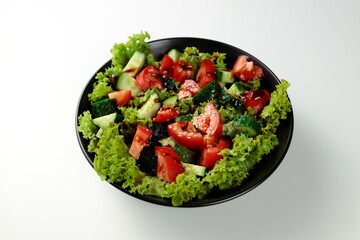 Vegetable salad of tomatoes, cucumbers, onions, lettuce dressed with aromatic dressing in a black plate on a white  background