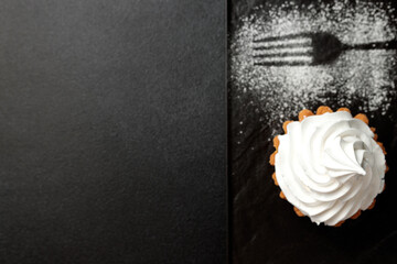 The sand basket is decorated with a high peak of protein cream. A tasty and sweet dessert stands on a black plate on a gray background