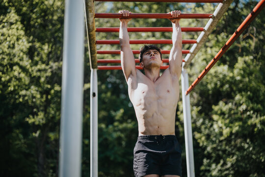 Athletic young man practicing calisthenics on monkey bars in an urban park. Displaying strength and endurance during outdoor fitness training - Powered by Adobe