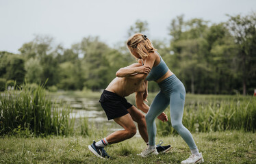 Athletic couple engaged in wrestling practice in the park. Active lifestyle, fitness training, and strength exercise