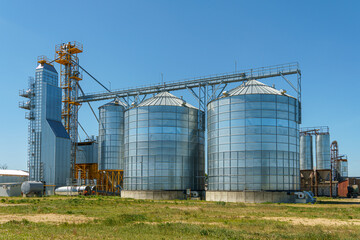Obraz premium silver silos on agro manufacturing plant for processing drying cleaning and storage of agricultural products, flour, cereals and grain. Large iron barrels of grain. Granary elevator