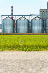 silver silos on agro manufacturing plant for processing drying cleaning and storage of agricultural products, flour, grain. A granary on the background of a road, a place for text or advertising.