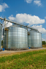 silver silos on agro manufacturing plant for processing drying cleaning and storage of agricultural products, flour, cereals and grain. Large iron barrels of grain. Granary elevator © Pokoman