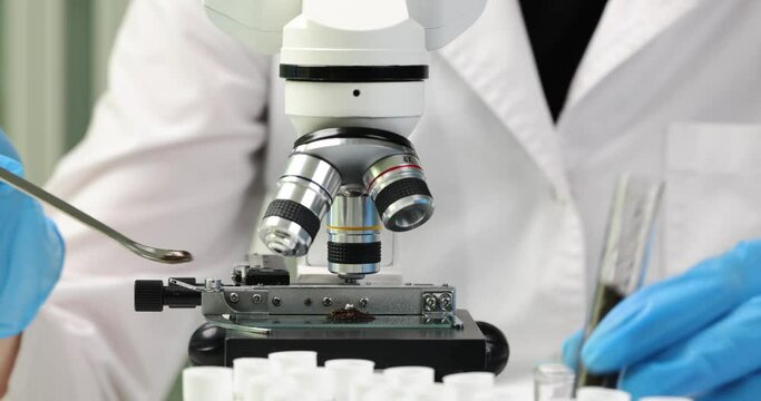 Laboratory worker takes soil from test tube and puts under microscope. Person in work uniform explores with device elements of earth soil