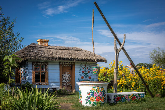 Zalipie, Poland - August 1, 2021:
Traditional wooden well in the garden. A bucket painted in colorful floral pattern. Yellow flowers in background. 