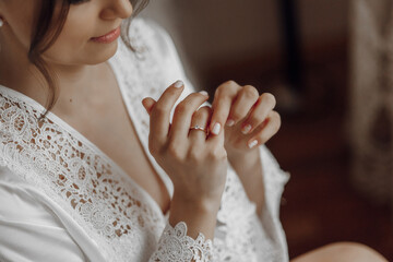 A woman is wearing a white gown and holding her hands together. She is wearing a diamond ring on her left hand