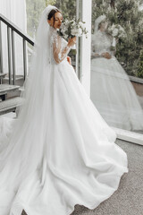 Obraz premium A bride is wearing a white wedding dress and holding a bouquet of flowers. The dress is long and flowing, and the bride is standing on a staircase. Concept of elegance and celebration