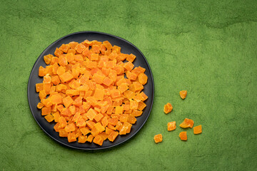 dried mango fruit diced - black ceramic palte on a green textured paper with a copy space