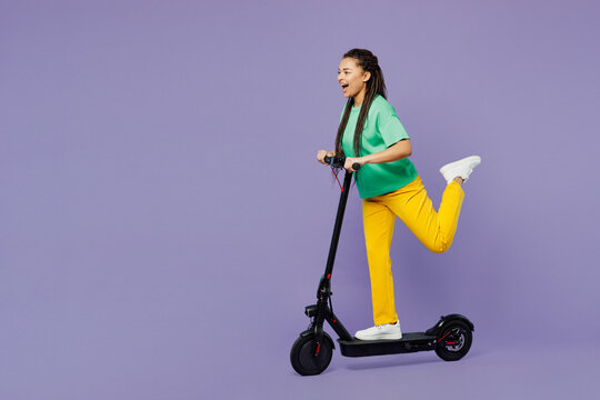 Full body young cool woman of African American ethnicity with dreadlocks wear green t-shirt casual clothes riding electric scooter isolated on plain pastel light purple background. Lifestyle concept. - Powered by Adobe