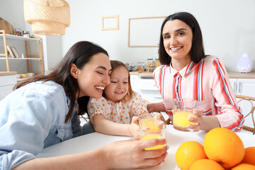 Young lesbian couple with adopted little girl drinking orange juice in kitchen