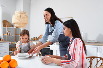 Young lesbian couple with adopted little girl having dinner in kitchen
