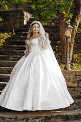 A woman in a white wedding dress is posing for a picture. She is standing on a set of stairs and is wearing a veil. Concept of elegance and celebration