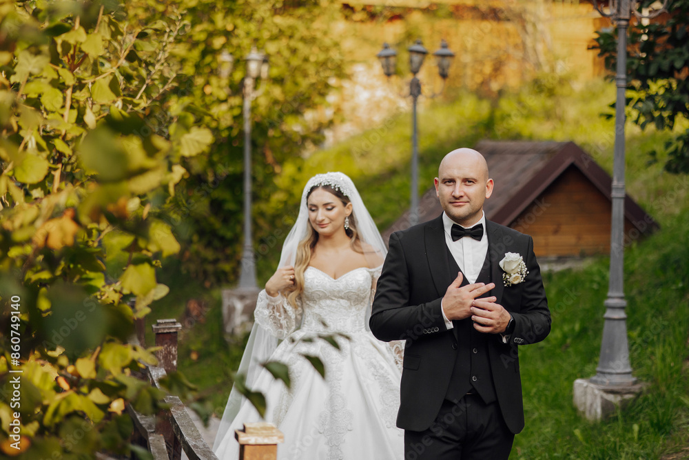 Wall mural a bride and groom are walking down a path in a garden. the bride is wearing a white dress and the gr