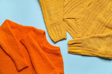 Stylish warm sweaters on color background, closeup