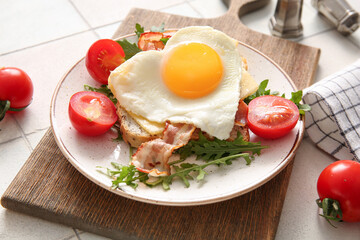 Plate with tasty fried egg, toast, bacon, tomatoes and arugula on light tile background, closeup