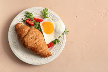 Plate with tasty fried egg, croissant, tomatoes and arugula on beige background