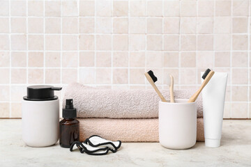 Set of bath supplies with toothbrushes on table against light tile wall