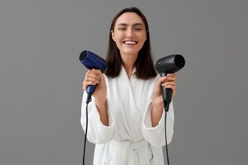 Beautiful young woman with hair dryers on grey background