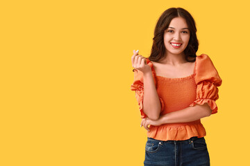 Happy young Asian woman showing heart gesture on yellow background. Valentine's Day celebration