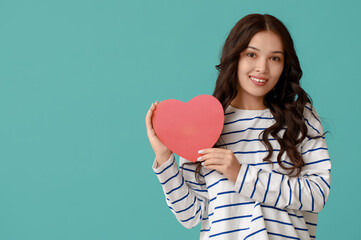 Beautiful young Asian woman with red paper heart on blue background. Valentine's Day celebration