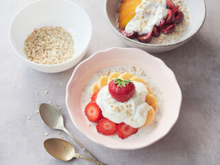 Delicious healthy dessert with oat porridge and yogurt, garnished with fresh fruits and served on bowls on gray table.
