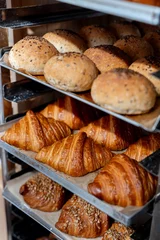 Fototapeten Close-up of freshly baked bread and croissants displayed on a rack in a bakery. Variety of baked goods © sergiophoto