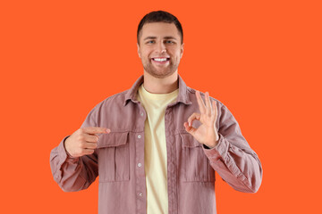 Handsome man pointing at OK gesture on orange background