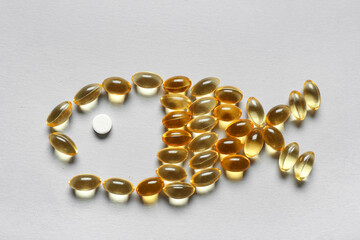 Fish shape made of capsules on grey background