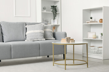 Interior of light living room with grey sofa, table and shelf units