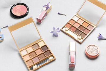 Eyeshadows palettes with lip glosses, highlighter and flower on white background