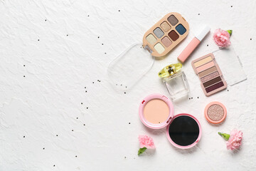 Makeup products with carnations, perfume bottle and sequins on white grunge background