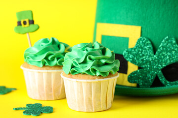 Tasty cupcakes with leprechaun hat and decor for St. Patrick's Day on yellow background