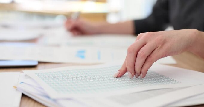 Female accountant makes financial report using spreadsheet with expenses. Employee with nude manicure runs hand down sheet to check data slow motion