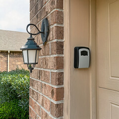 lamp on the house exterior wall next to a key security lock box attached to garage door trim.