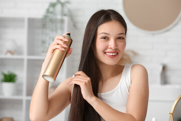 Beautiful young happy woman applying hair spray at home