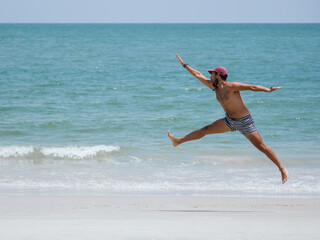 Energetic Young Man Jumping on the Beach with arms and legs stretched