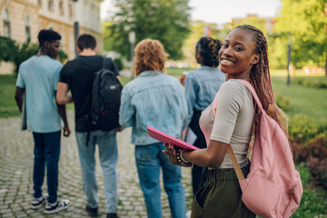 Happy diverse female student at campus looking over shoulder and smiling