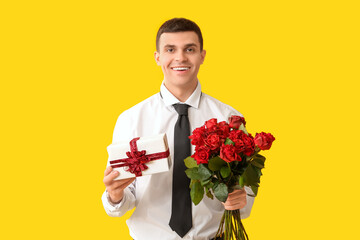 Handsome man with gift box and red roses on yellow background